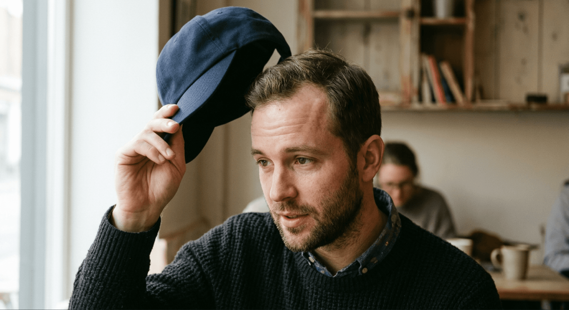 Man lifting his cap to reveal a receding hairline